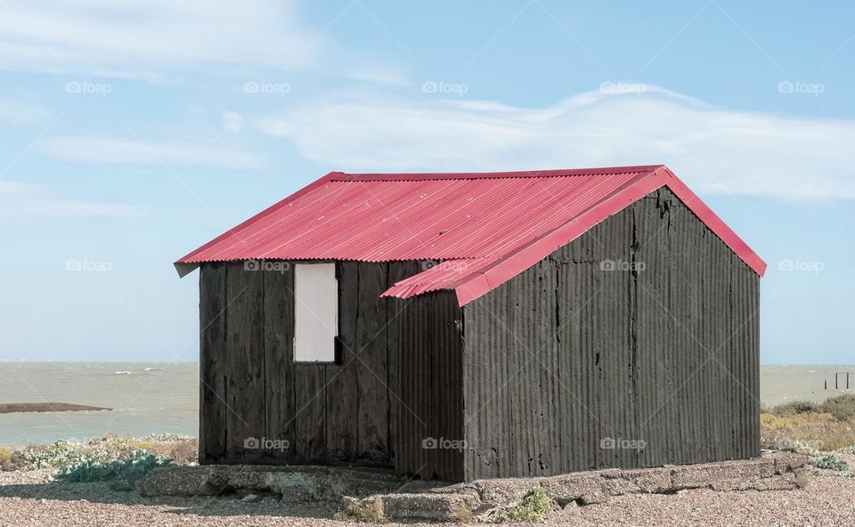 Red roof of a corrugated iron shack on the beach has been faded to a shade of magenta