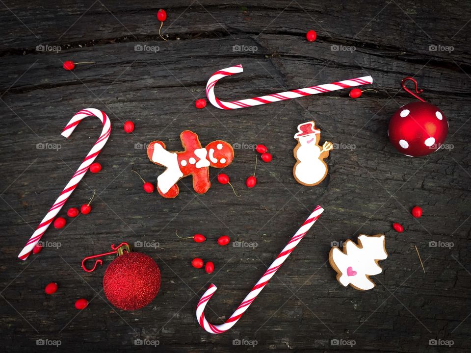 Flat lay of red and white Christmas decorations consisting of candy canes,gingerbread,red globes and red berries on rustic wooden table