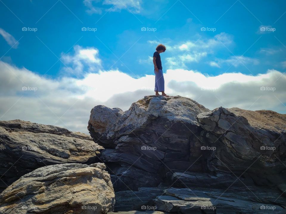 Boy standing atop a beach boulder