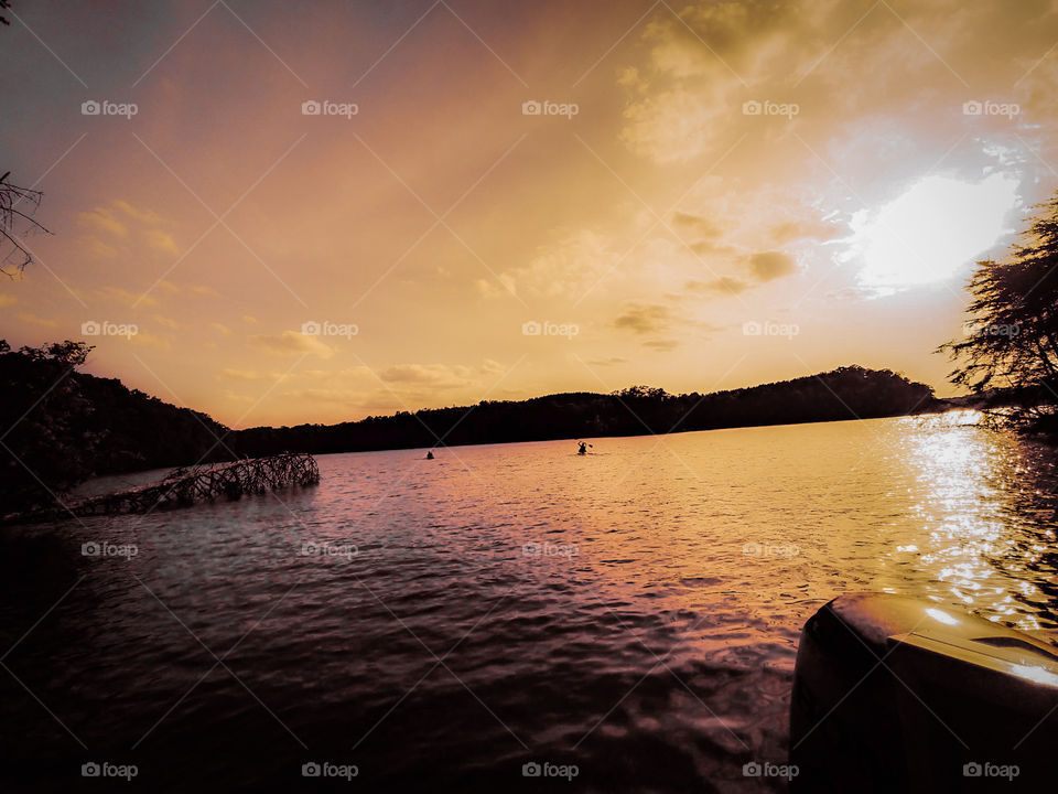 kayakers off in the distance in lake with golden hue sunset beaming down.