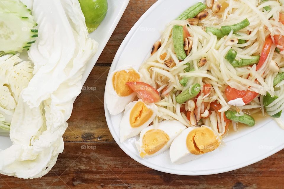 Thai salad or green papaya salad  (som tam) with selective focus on the salty eggs. served with sided vegetables. clean diet and clean food concept. healthy lifestyle.local north-east of Thailand food
