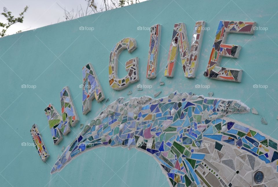 A blue wall with mosaic tile spelling the word IMAGINE