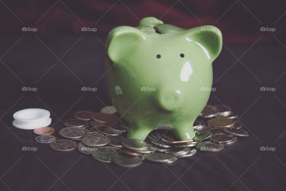 A green piggy bank on top of a pile of coins