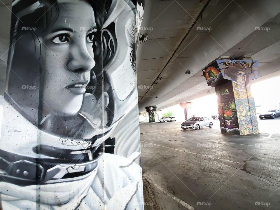 Street art:  Black and white portrait of a female astronaut on a cement highway bridge pillar.