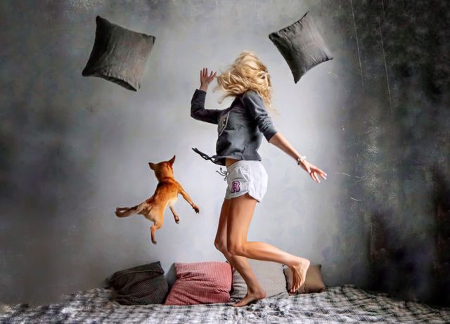 young woman jumping on the bed with her dog