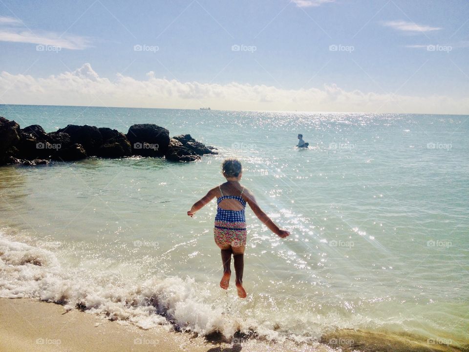 Little girl jumping in wave in ocean during a beautiful and sunny day! Water is clear and waves are perfect for jumping in!