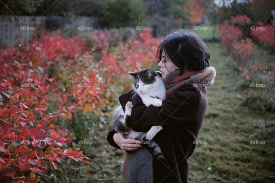 A young girl on the background of autumn foliage holding a cat in her arms