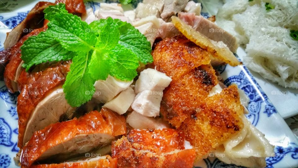 Roast duck and pork pieces on a plate. Some crackling skin portions can be seen on the roast pork. Classic Chinese style cuisine.