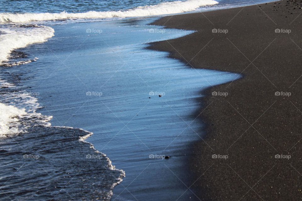 Close up blue waves splashing on a black sand beach