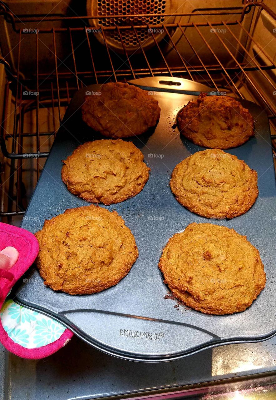 Hot homemade muffins in pan held by potholder coming out of oven, ready to eat.