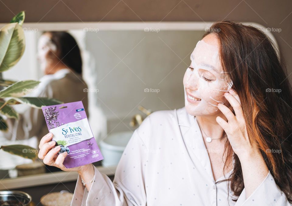 Woman with long hair with sheet mask st. ives in hands in bathroom at home 