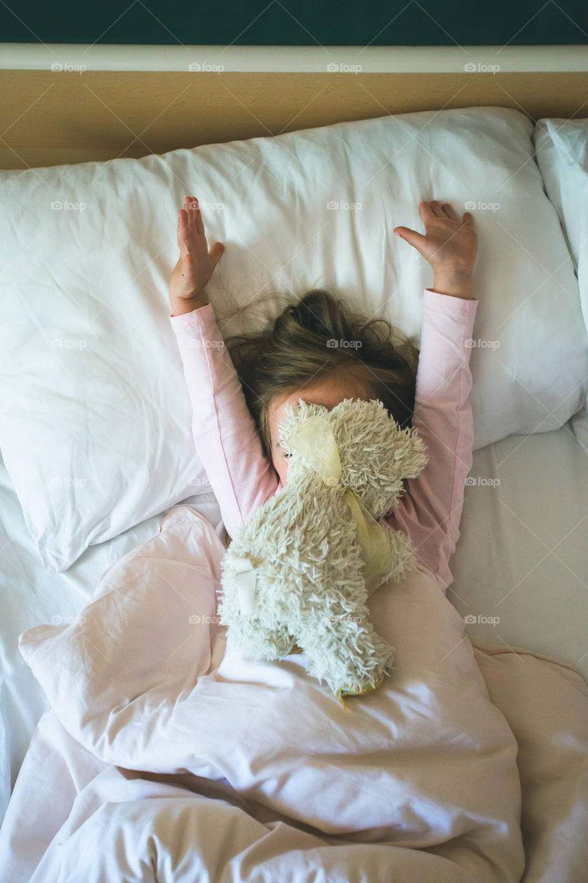 Little girl lying in a bed with teddy bear at the morning