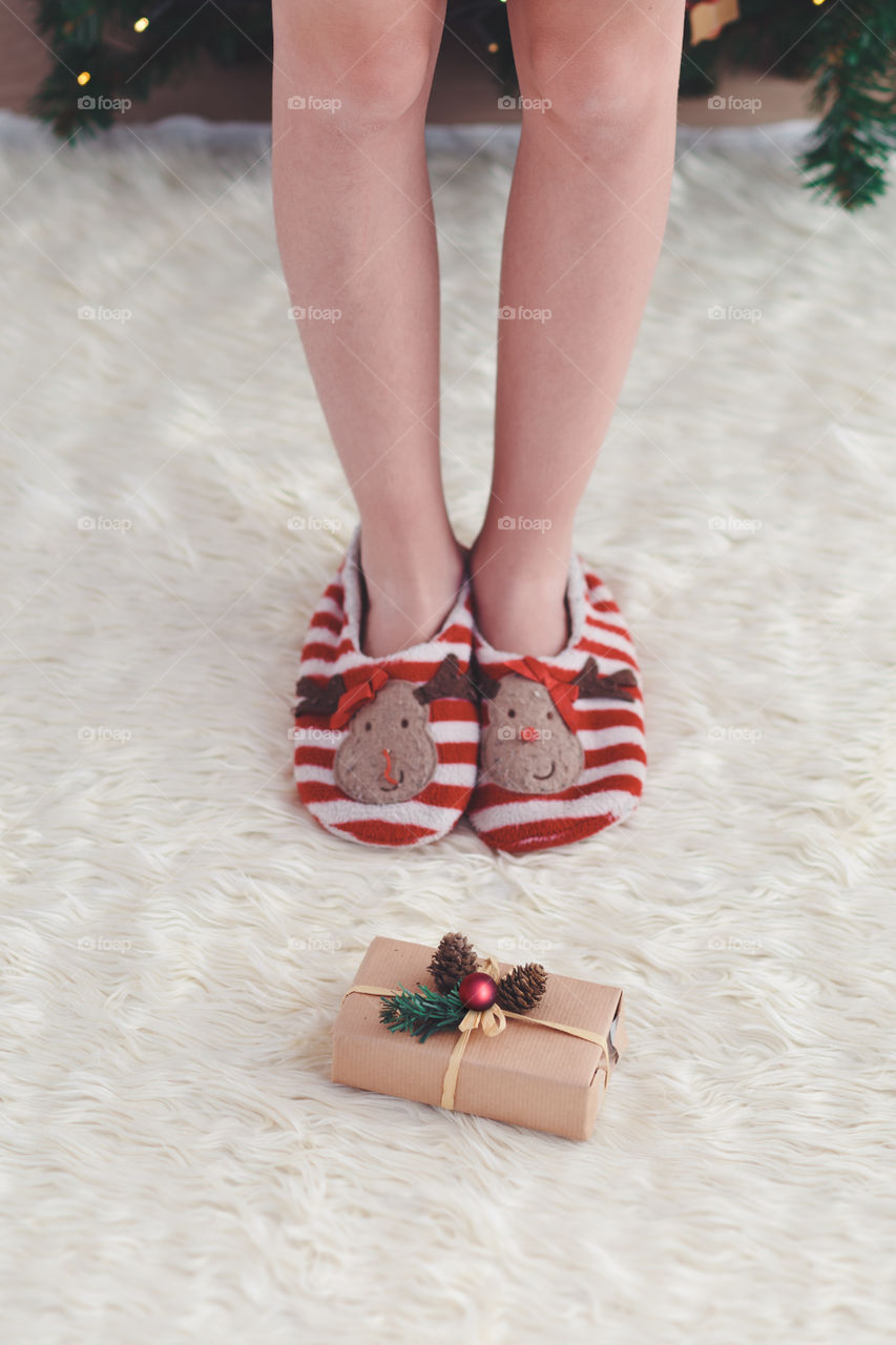 Girl standing by Christmas gift put near tree on a carpet