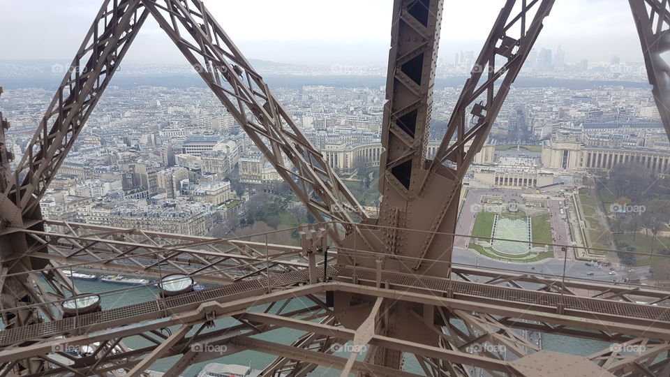 View from above, looking out elevator window from inside the Eiffel tower, seeing through to the city and gardens of Paris, France, below.