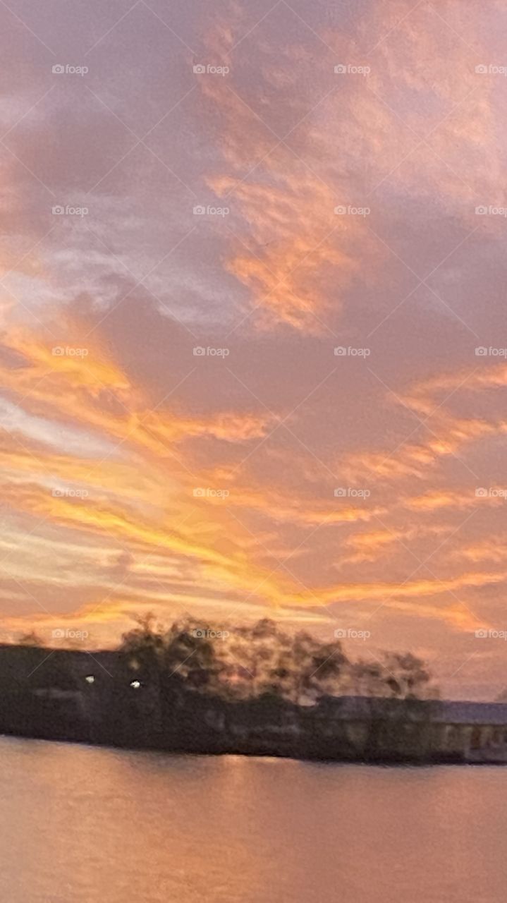 Sundown Completed Sky is opening up. Blistering Orange Slivers along with Yellows upper atmosphere bleeding down to the lower with Grays Blues Violets tops of high clouds getting into the act by opening up.