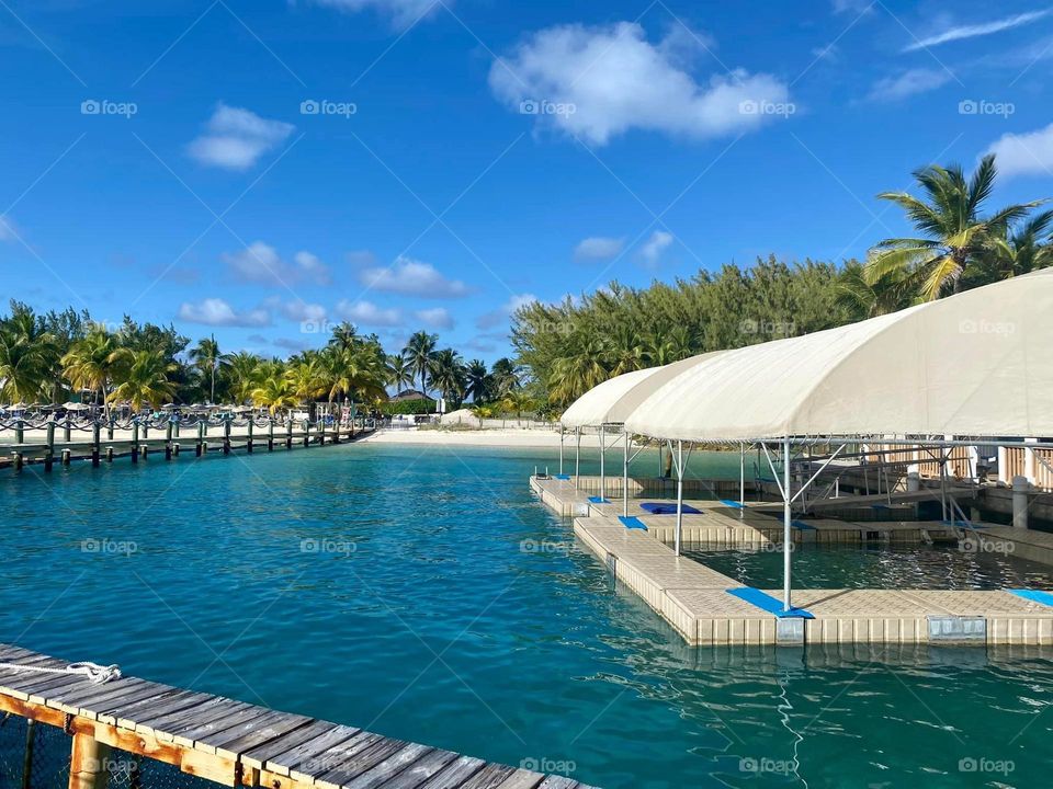 A wooden dock walkway is surrounded by the turquoise waters and sandy shores of this beach island. 