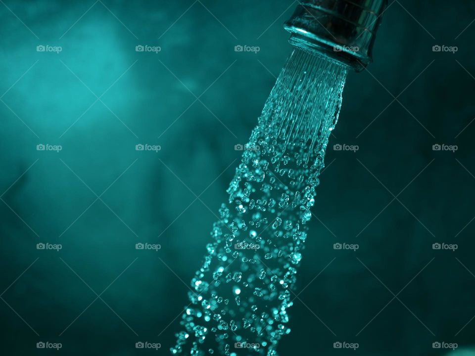 Water falling down from faucet and droplets from spray, turquoise color