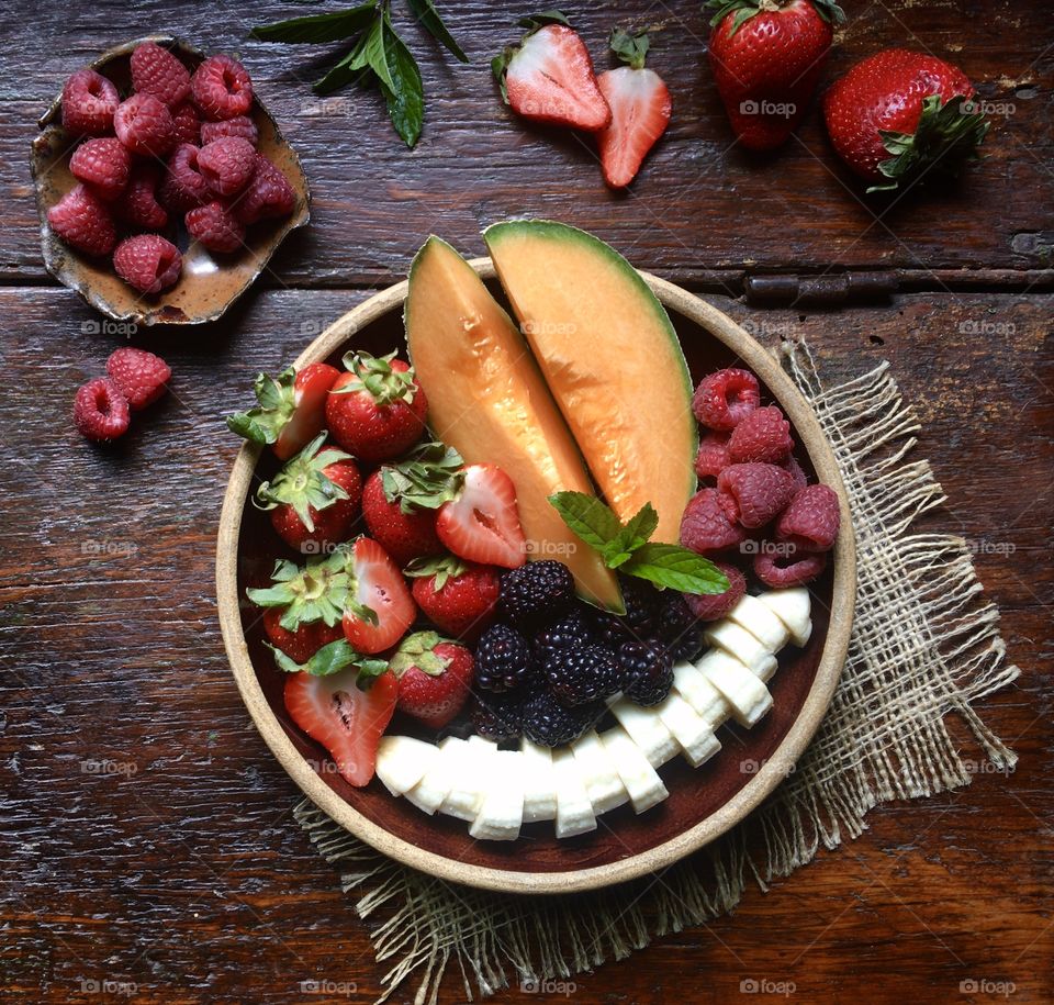 Fresh fruit plate with strawberries, cantaloupe, raspberries, blackberries and banana slices on a rustic wood table.