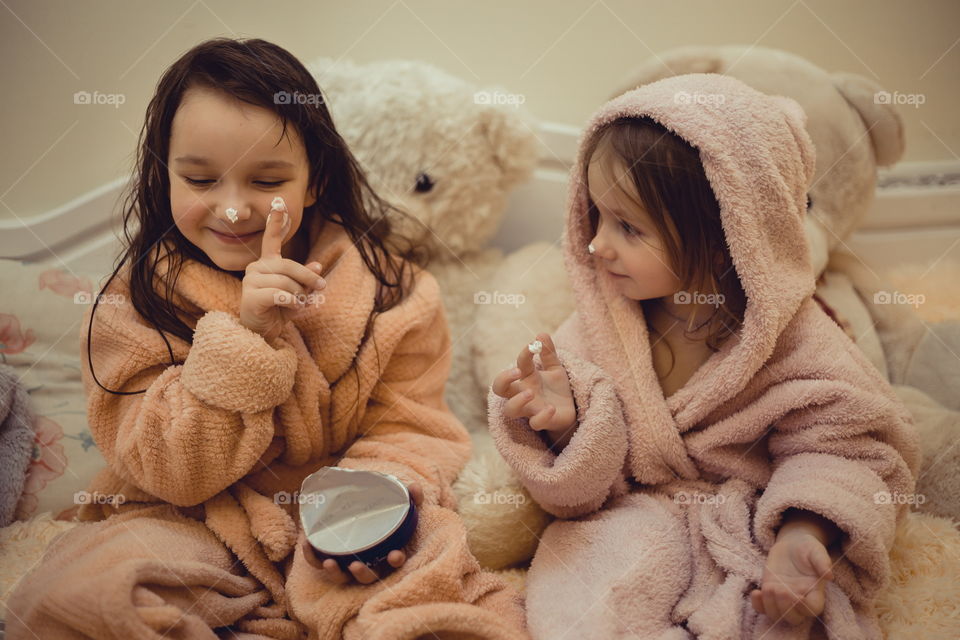 Little sisters in bathrobe with cream