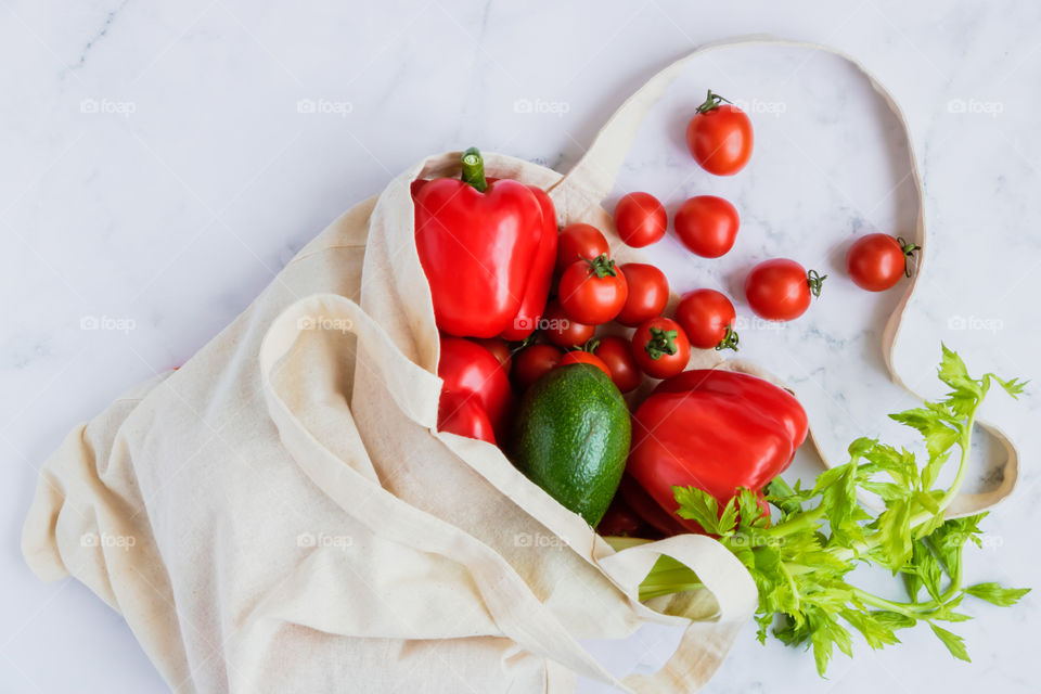 Top view to red and green vegetables in linen reusable bag on marble background. Eco-friendly concept.