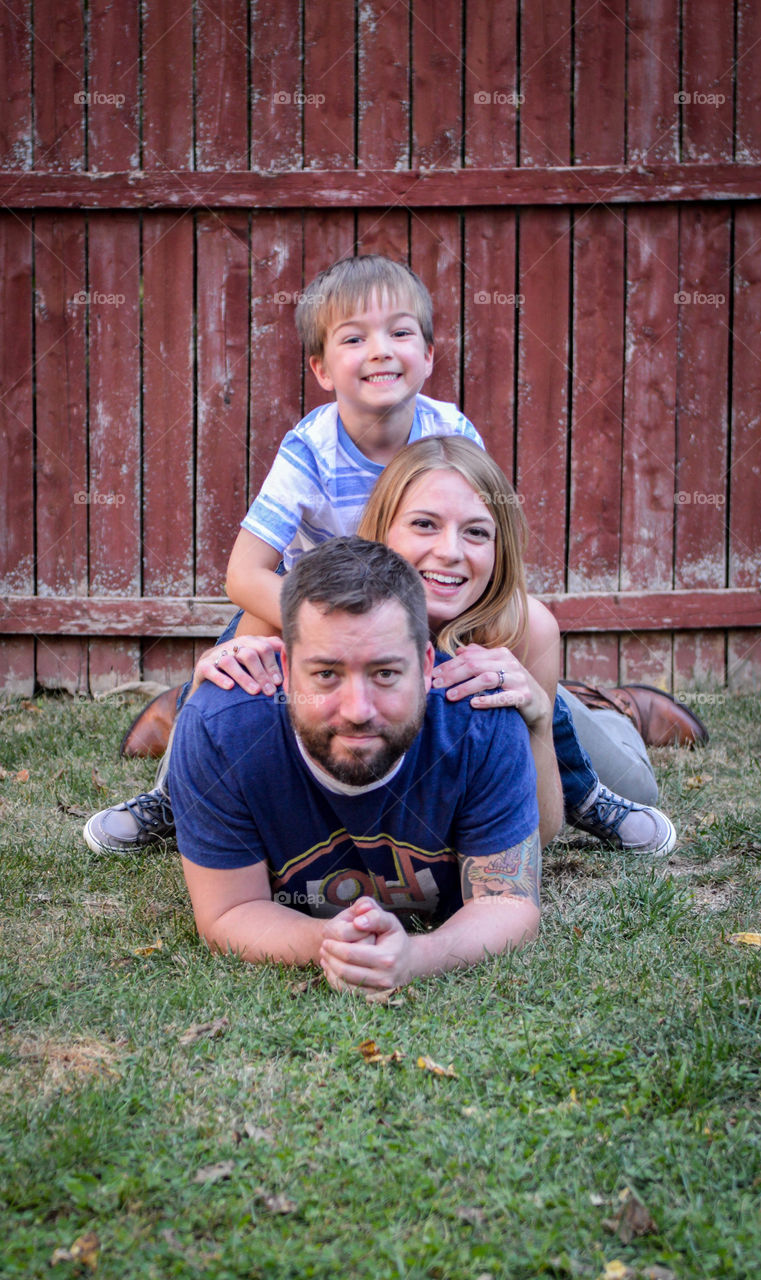 Family of three piled on top of one another in the grass outdoors
