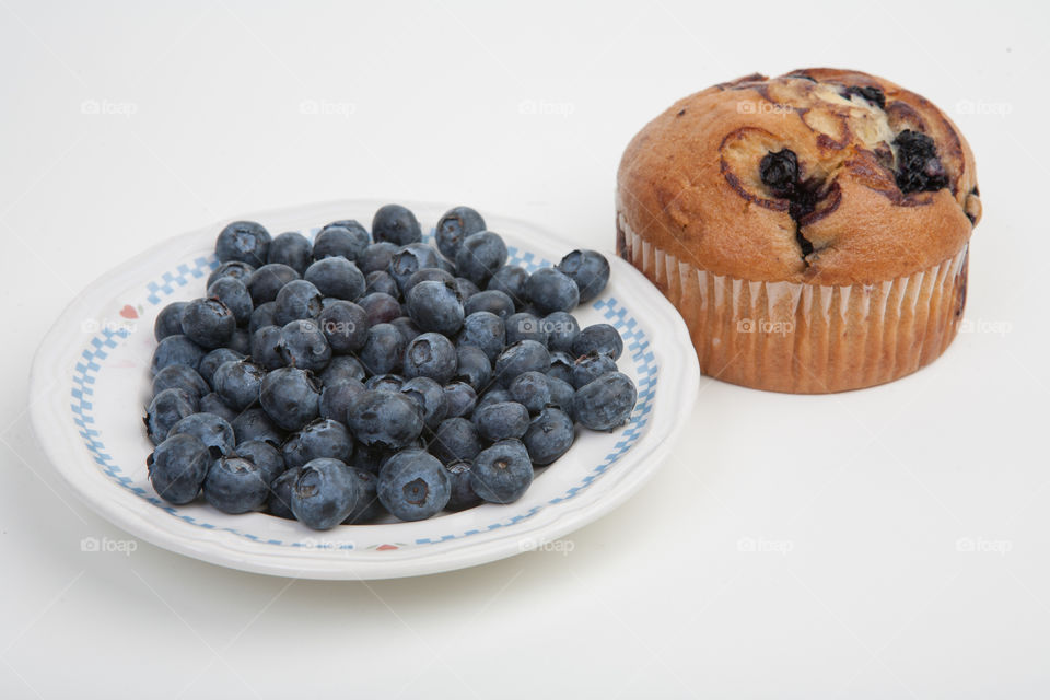 Blueberries in bowl and blueberry muffin on white background