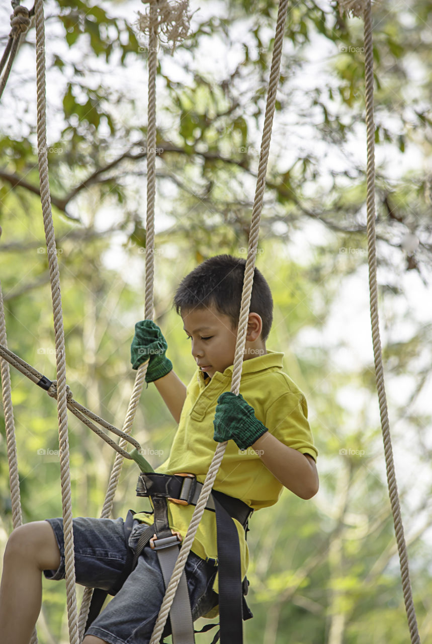 Asean boy nodes the rope and smiling happily in camp adventure Background blurry tree.