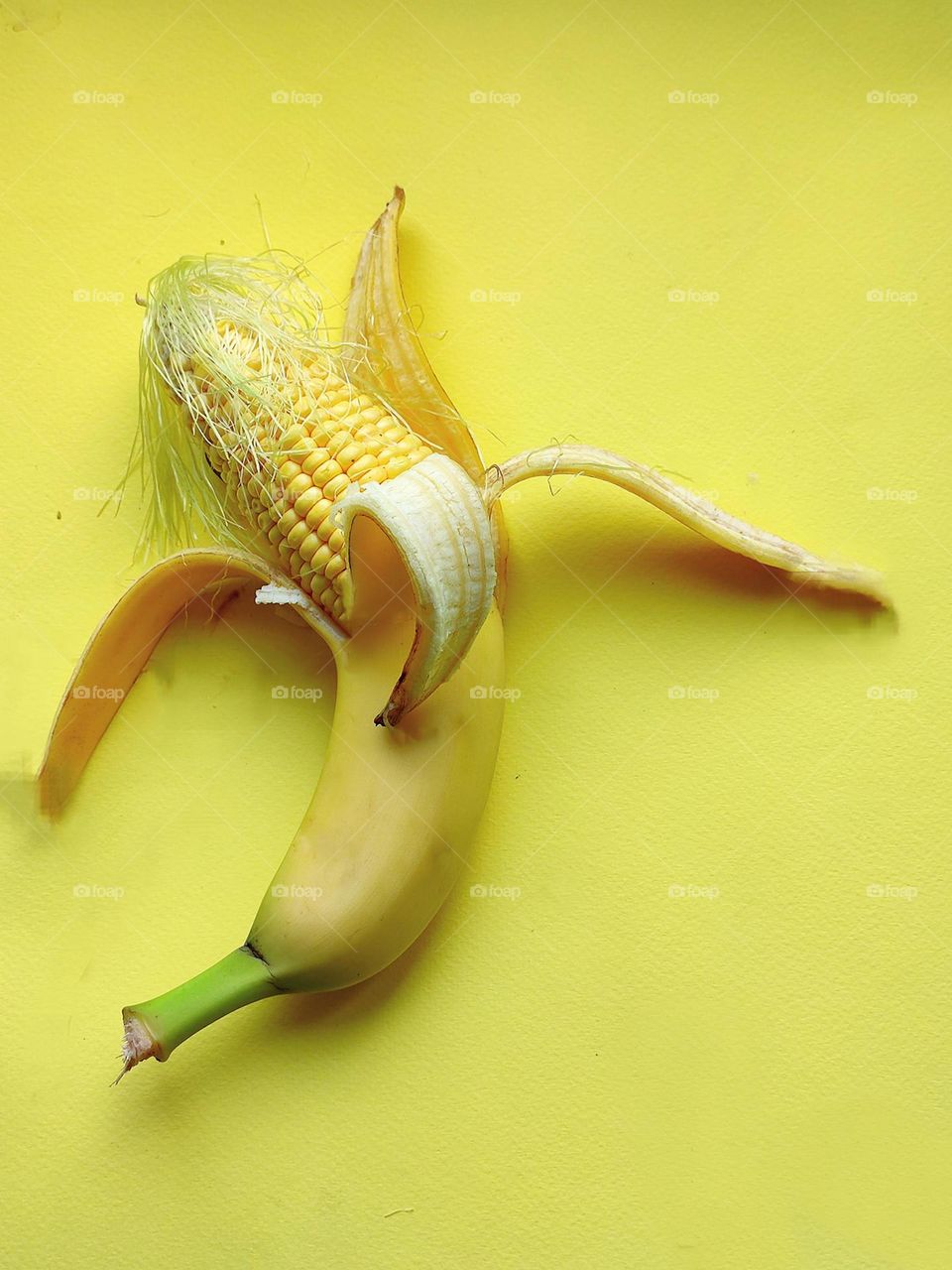 On a yellow background, half a banana connected to half a corn