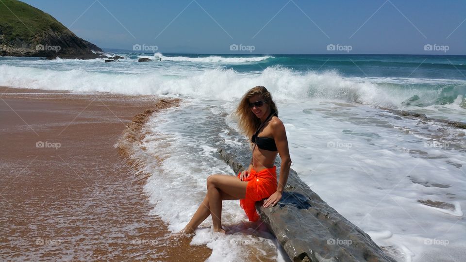 blonde girl near Cantabria sea. blonde girl in black bikini sitting near waves on Cantabria sea, North Spain