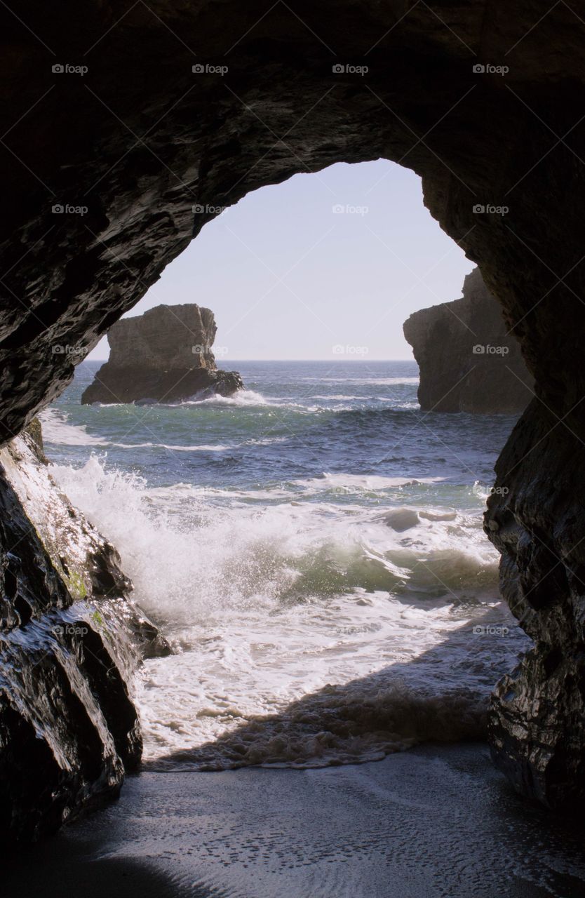 Gentle waves crashing through a small sea cave at low tide at Sharktooth Beach in Davenport, California on a clear, bright sunny day