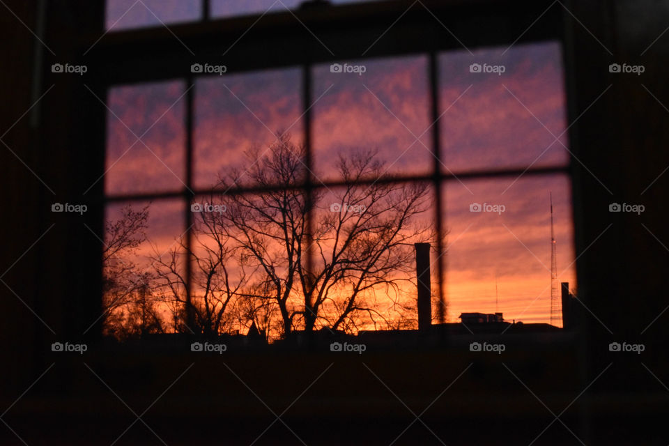 Beyond the frame of an apartment window, a beautiful sunset ends a still day. 