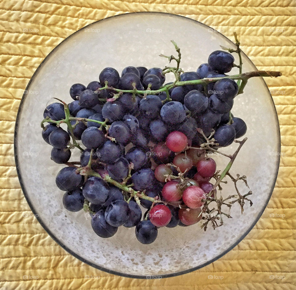 A bowl of black and red grapes on a quilted yellow tablecloth 