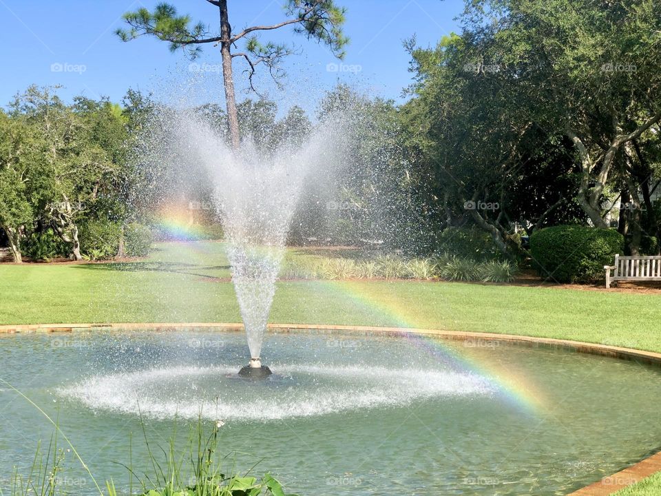 Water droplets from a park fountain create a bright rainbow on a sunny day outside