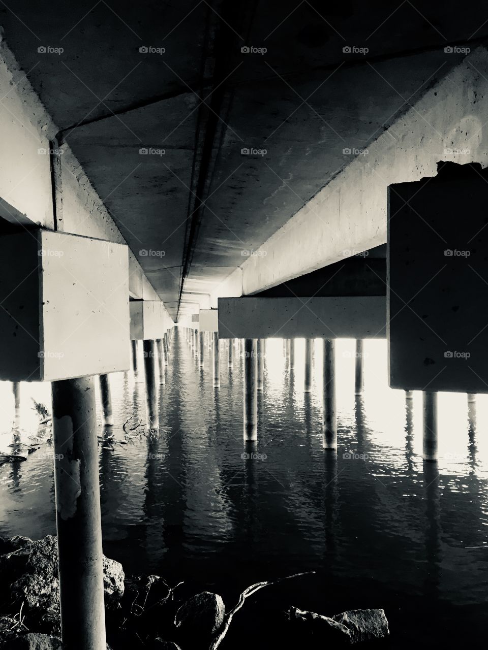 Black and white of pillars holding up the bridge over the river 