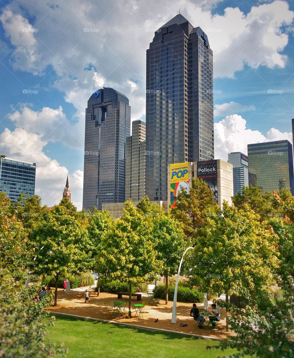 People enjoying Klyde Warren Park under the skyscrapers of downtown Dallas Texas USA on a sunny summer fluffy white cloud filled day a local treasure