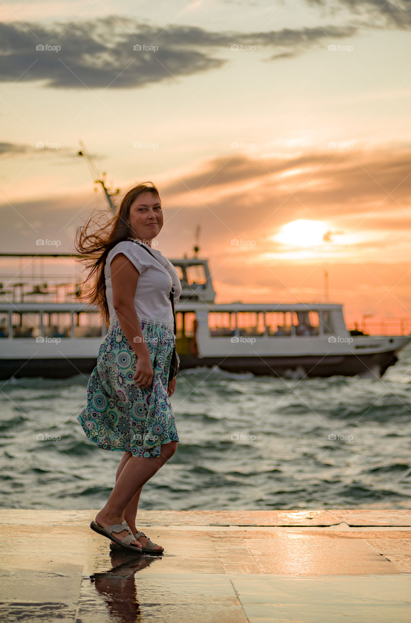 Warm summer evening, during sunset, a girl stands on the seashore and a boat floats in the background