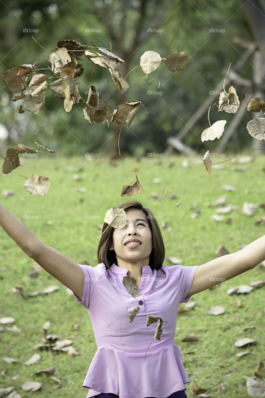 Portrait of Asean woman throwing dry leaves on the lawn in a park.