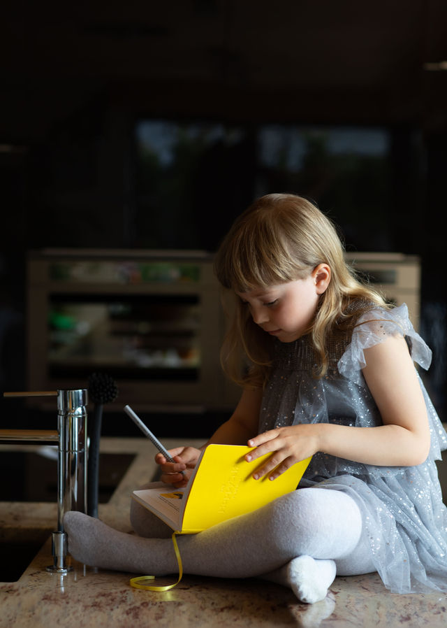 Girl of 6 years is learning her HappySelf journal sitting on a kitchen table top.