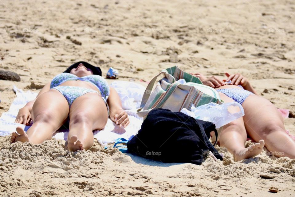 Two girls lie down on the beach getting tan and laughing 