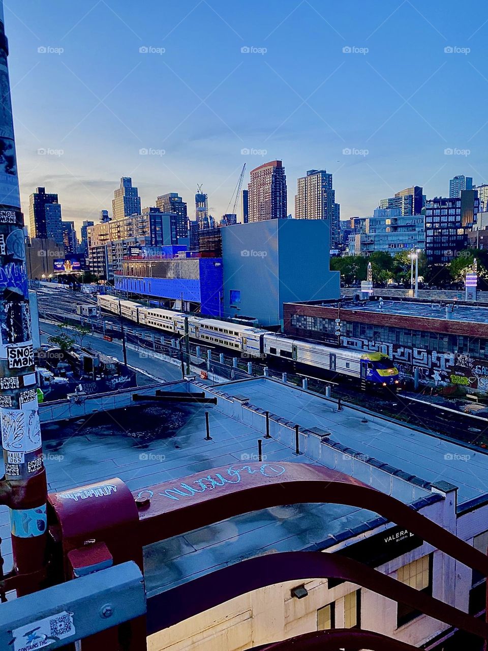 This is the view from the top of the staircase of the “Pulaski Bridge” on the LIC, Queens side of the bridge. A “Long Island Railroad” train can be seen approaching us on the tracks as well as the “Manhattan” skyline. 2023. Hypnotic Productions