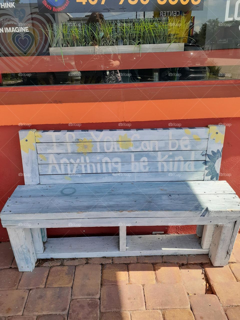 A pale blue bench sits outside a restaurant in Orlando. Words on the bench say, "If you can be anything, be kind. "