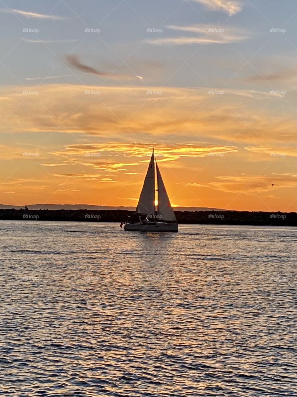Beautiful sunset over the Newport Beach Jetty from Corona del Mar with a sailboat in front of it