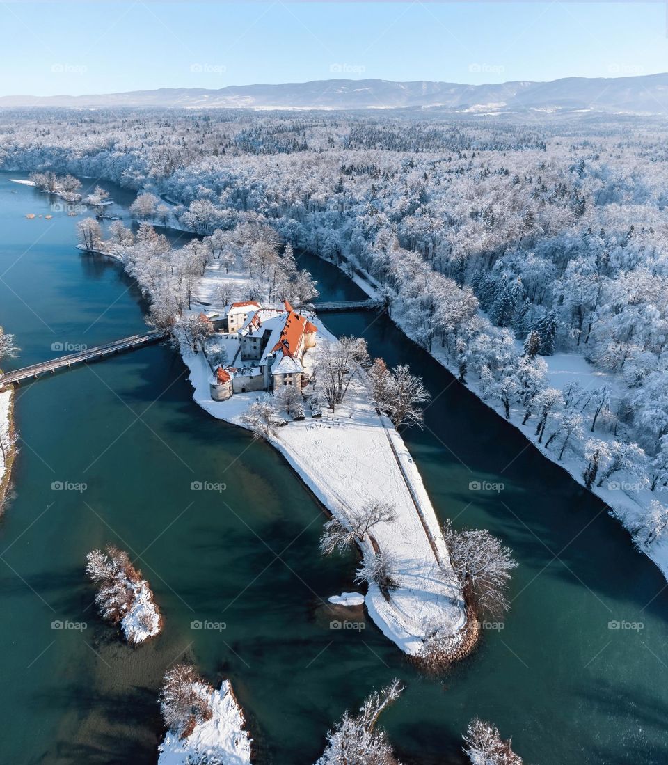 Majestic aerial view of castle on river island surrounded by winter forest with fresh snow. Otocec castle on Krka river in Slovenia.