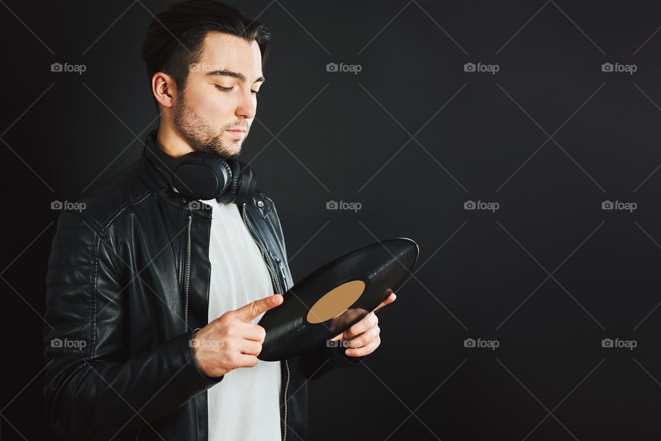 Handsome man looking at vinyl record. Rock style. Vintage music style. Male wearing black jacket holding turntable plate standing on black background. Retro music. Classic audio. Copy space right