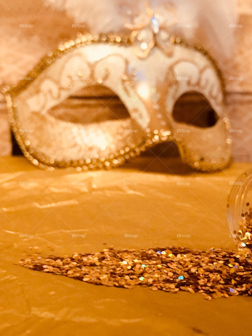 Close up view of gold glitter spilled onto gold tissue paper with a Venetian masquerade mask 