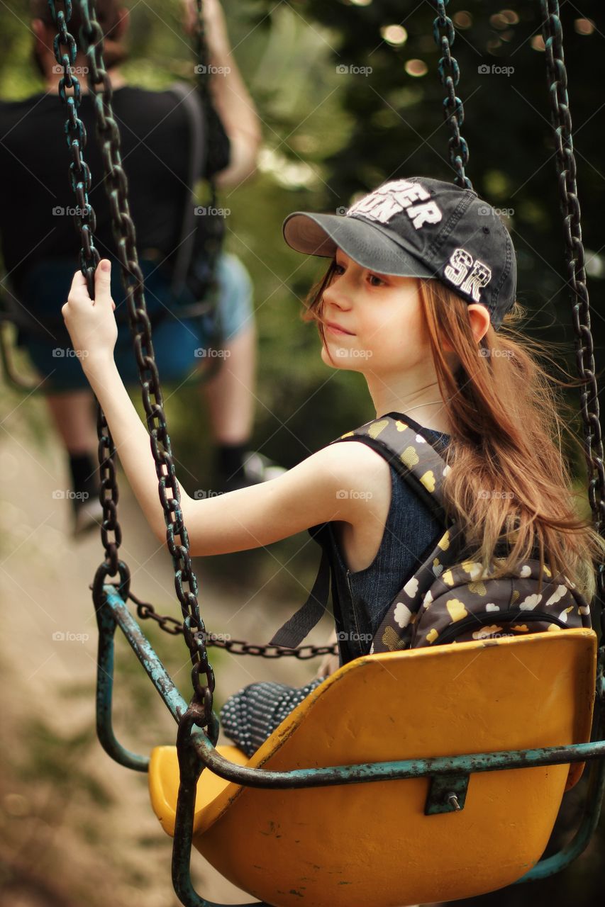 Girl in a cap rides on a chain carousel in the park