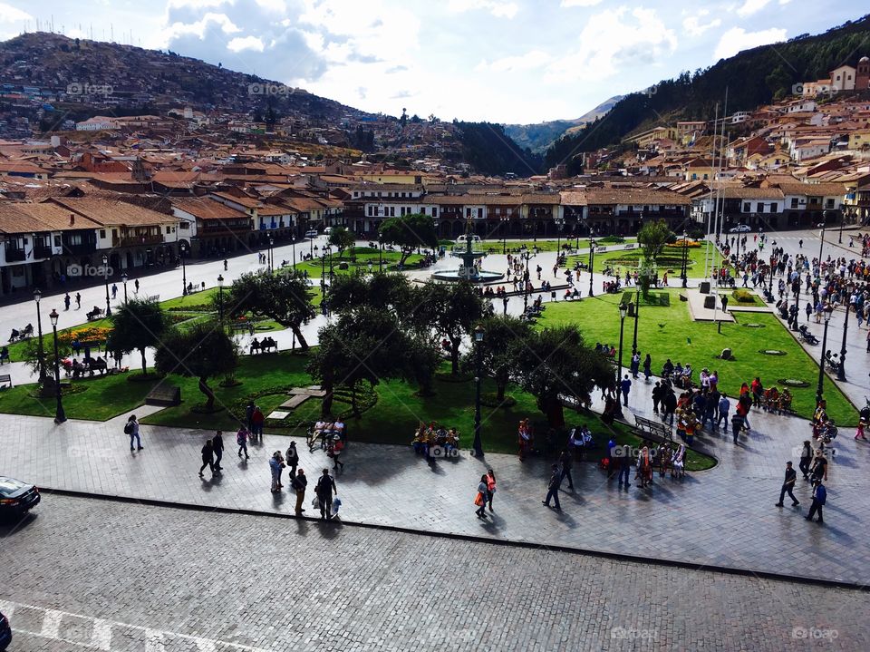 The lush main plaza in Cuzco, showing locals and tourists moving about on a bright day. 