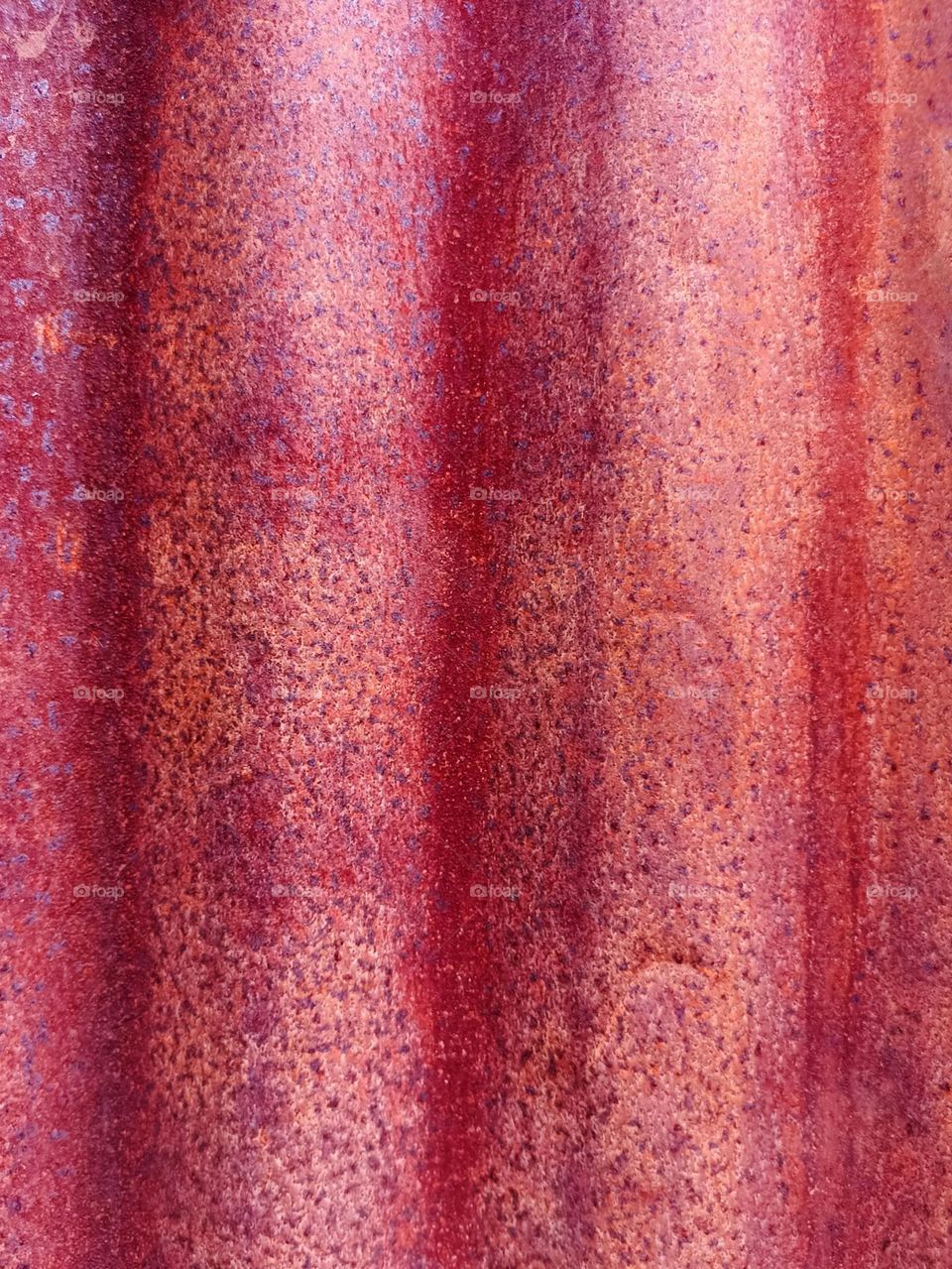 Close-up of the texture and color of a surface that appears to be oxidized metal, with shades of red, purple, and orange