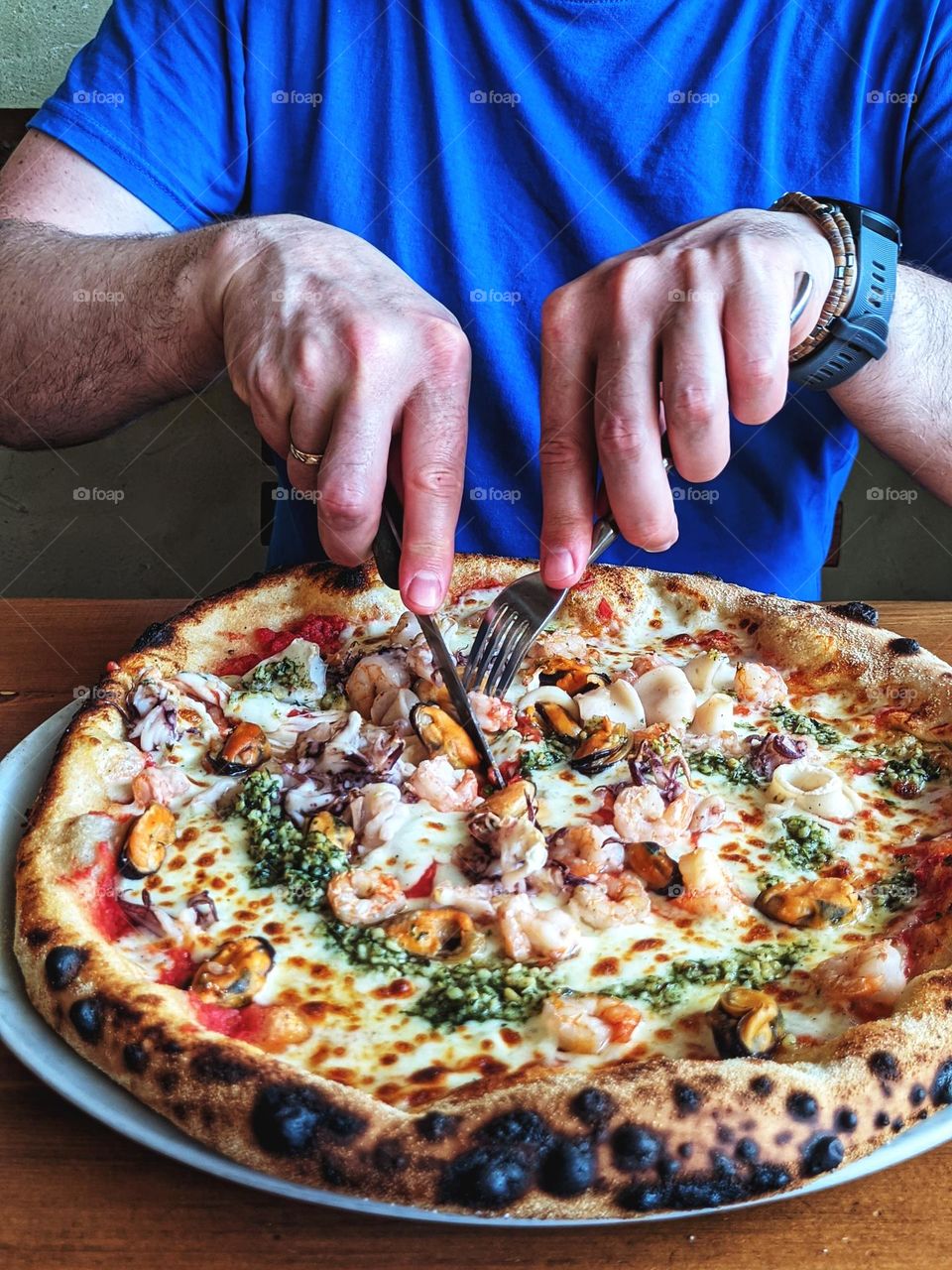 Food background.  Top view of man hands with fork and knife.  Eating delicious Italian pizza with seafood.