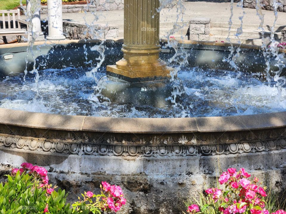 water splashing in base of fountain surrounded by pink flowers